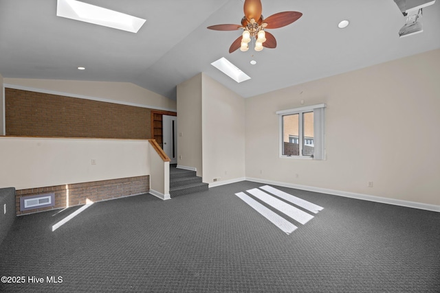 empty room with vaulted ceiling with skylight, dark colored carpet, a ceiling fan, baseboards, and visible vents