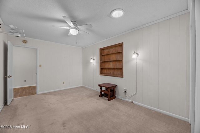 carpeted empty room featuring built in features, baseboards, a ceiling fan, and a textured ceiling