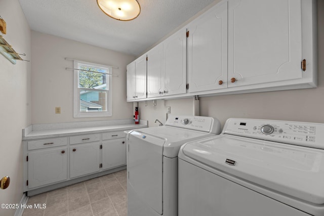 clothes washing area with a textured ceiling, cabinet space, and washer and clothes dryer