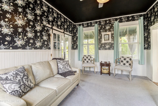 carpeted living room featuring wallpapered walls, wainscoting, a ceiling fan, and crown molding