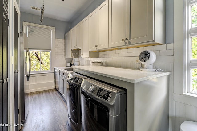 clothes washing area with healthy amount of natural light, washer and dryer, and wood finished floors