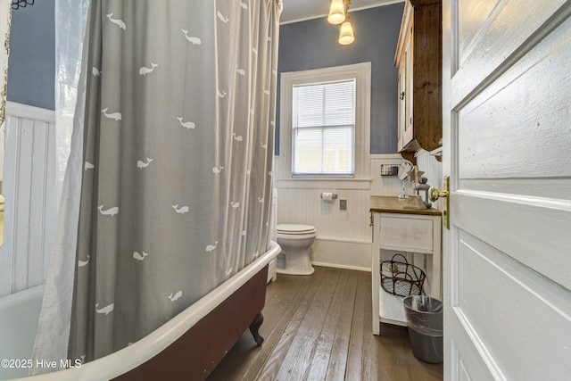 full bathroom featuring wainscoting, toilet, hardwood / wood-style flooring, shower / bath combo with shower curtain, and crown molding