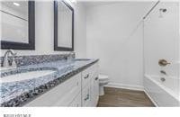 full bath with double vanity, toilet, bathtub / shower combination, baseboards, and wood finished floors