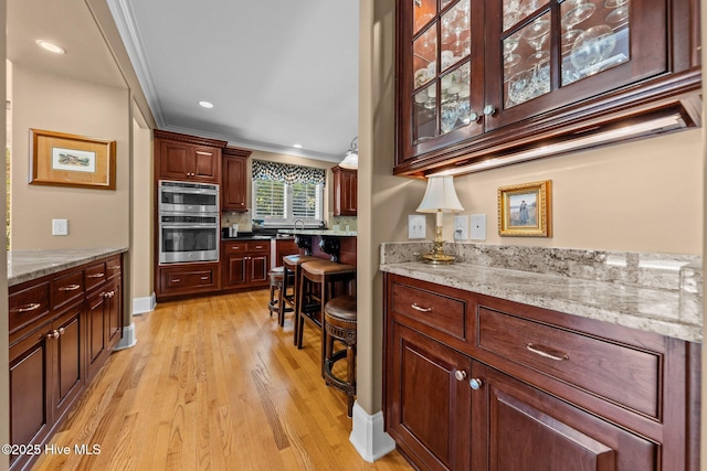 kitchen featuring crown molding, light wood-type flooring, glass insert cabinets, light stone counters, and recessed lighting