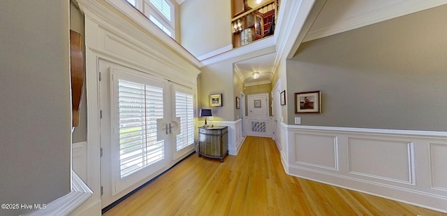 hall featuring light wood finished floors, wainscoting, french doors, a towering ceiling, and a decorative wall