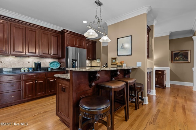 kitchen featuring high end refrigerator, crown molding, a kitchen bar, light wood-style flooring, and baseboards