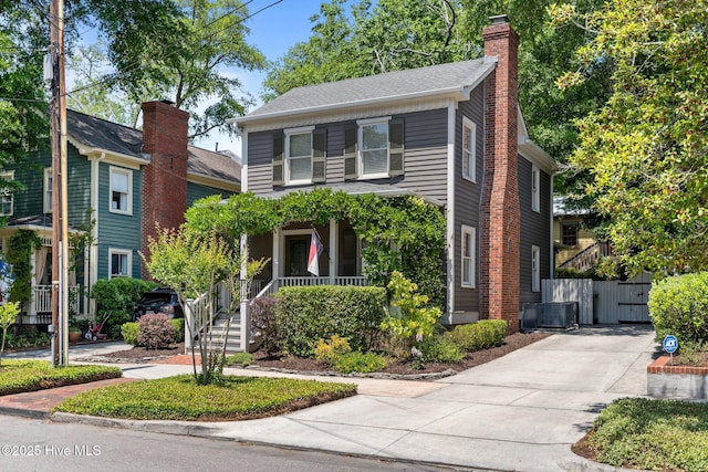 traditional home with covered porch, a chimney, cooling unit, and driveway