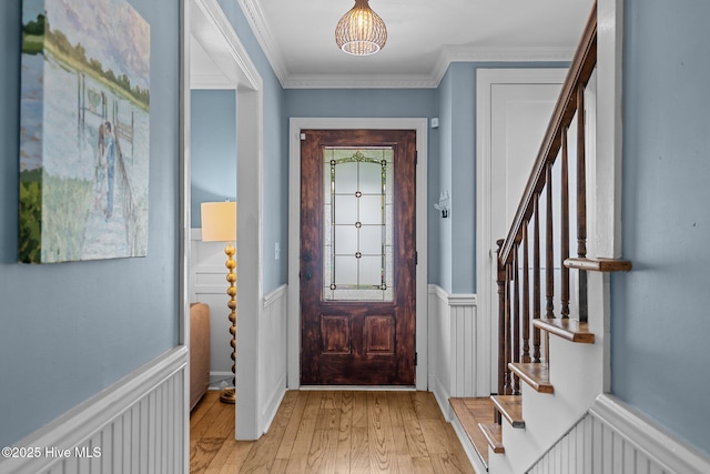 entryway with light wood-type flooring, ornamental molding, stairs, and a wainscoted wall