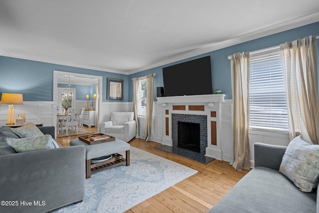 living area with an inviting chandelier, crown molding, wainscoting, wood finished floors, and a fireplace