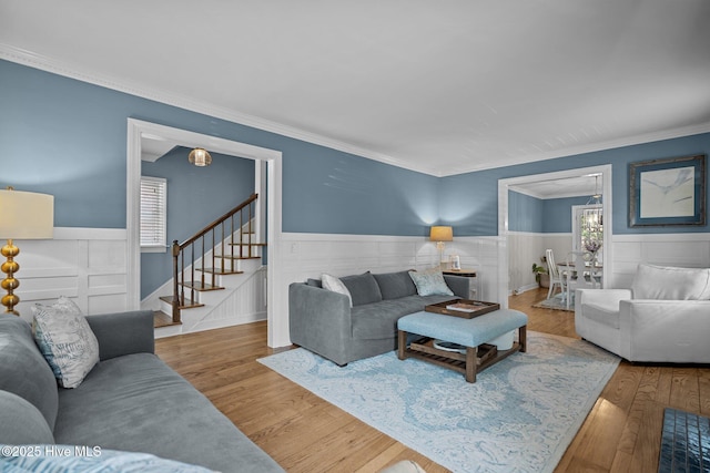 living room with crown molding, stairs, wood finished floors, a wainscoted wall, and a chandelier