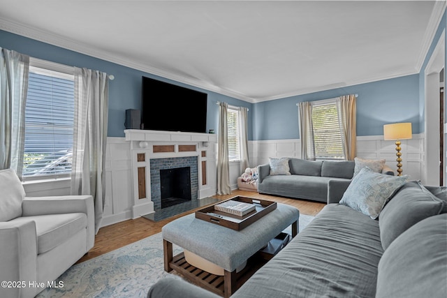 living room featuring ornamental molding, wainscoting, wood finished floors, and a fireplace