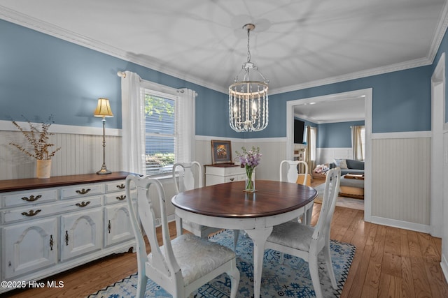 dining room featuring an inviting chandelier, light wood-style flooring, wainscoting, and ornamental molding