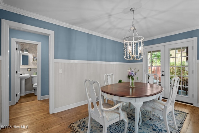 dining room with an inviting chandelier, ornamental molding, wainscoting, light wood-type flooring, and french doors
