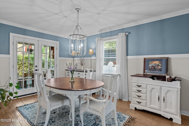 dining area with light wood-style floors, a wainscoted wall, french doors, and a chandelier