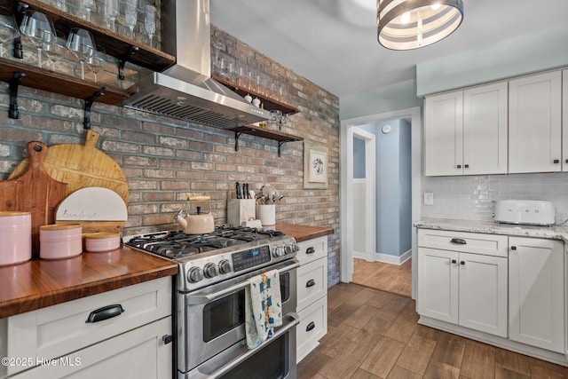 kitchen with wall chimney range hood, tasteful backsplash, double oven range, and butcher block countertops