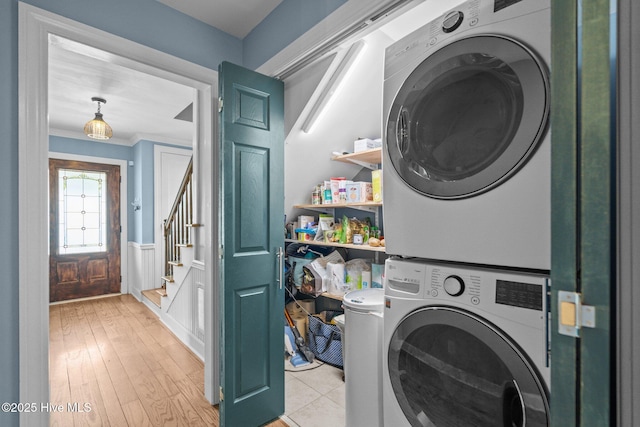 laundry area featuring stacked washing maching and dryer, crown molding, laundry area, and wainscoting