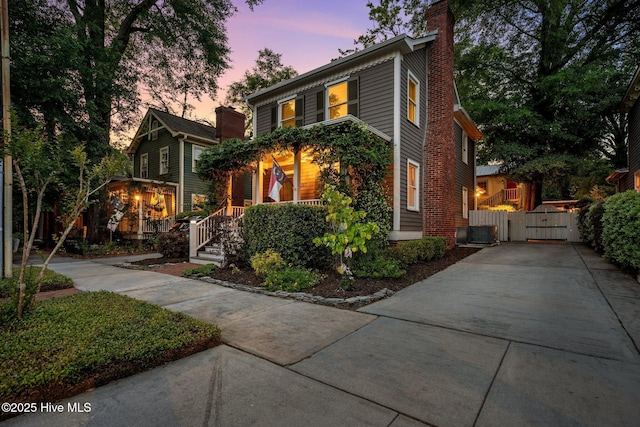 traditional-style home with central AC unit, a gate, a chimney, and concrete driveway