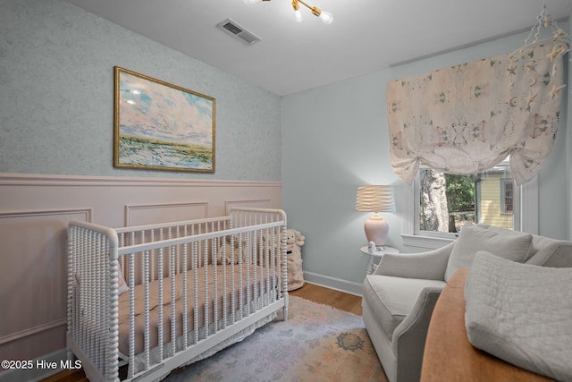 bedroom with visible vents, a nursery area, wood finished floors, a wainscoted wall, and baseboards