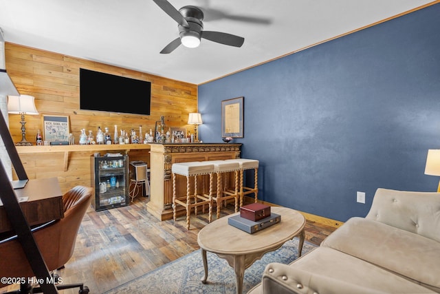 living area featuring wine cooler, wood finished floors, ceiling fan, wooden walls, and a dry bar