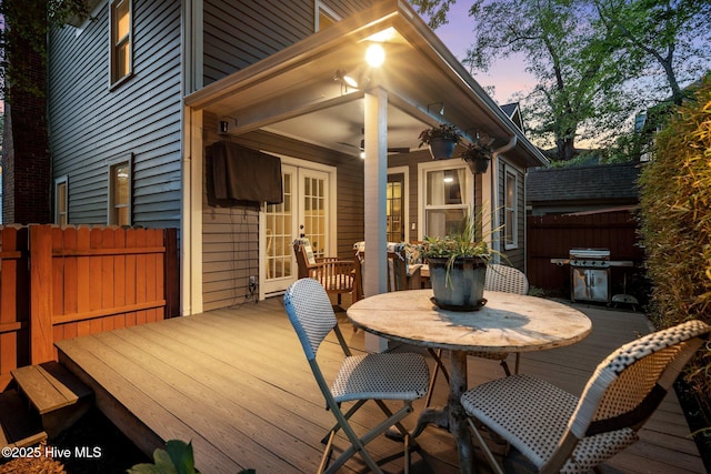 deck at dusk featuring area for grilling, fence, french doors, and outdoor dining area