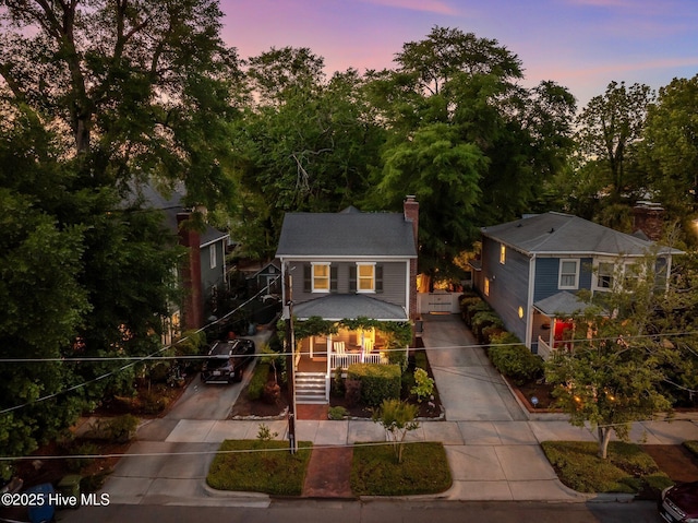 view of front of house with a chimney, concrete driveway, a porch, and stairway