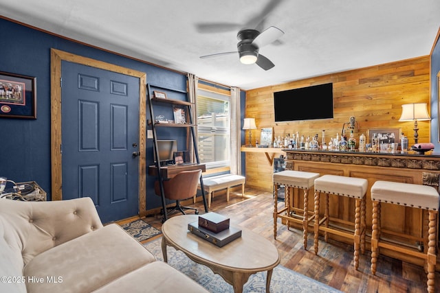 living area with a dry bar, ceiling fan, wooden walls, and hardwood / wood-style floors