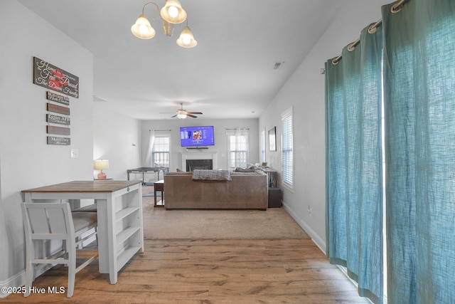 living area with a fireplace, ceiling fan with notable chandelier, baseboards, wood finished floors, and visible vents