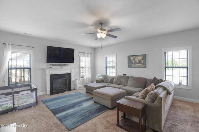 living area with a fireplace with flush hearth, baseboards, ceiling fan, and carpet