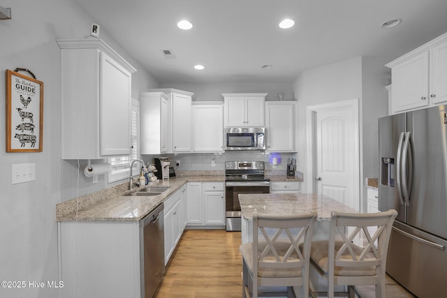 kitchen featuring a sink, light stone counters, stainless steel appliances, and white cabinetry
