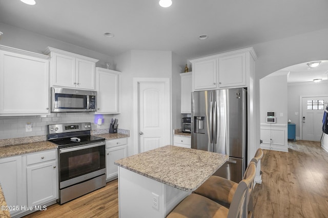 kitchen with decorative backsplash, white cabinets, arched walkways, light wood finished floors, and stainless steel appliances