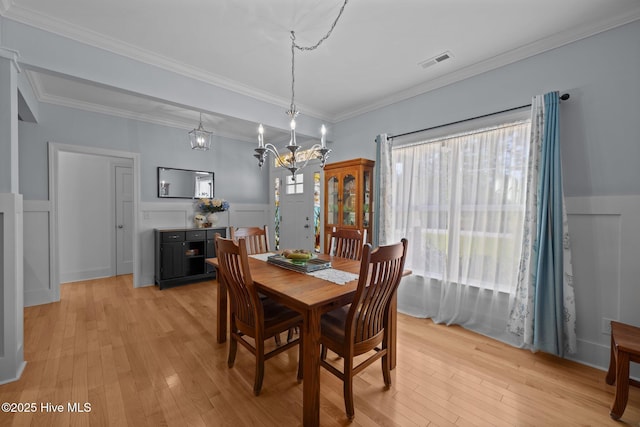 2312 Caracara Dr, New Bern, NC 28560 - dining room featuring light wood-style flooring, a chandelier, a wainscoted wall, and crown molding