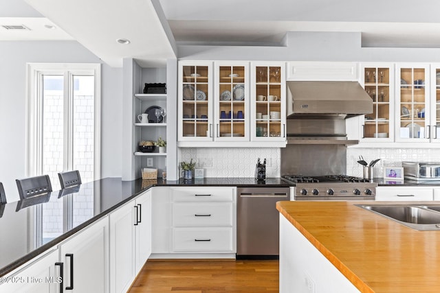 kitchen featuring stainless steel dishwasher, visible vents, ventilation hood, white cabinets, and backsplash