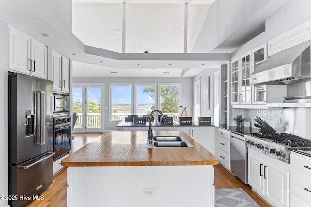 kitchen featuring wall chimney range hood, a sink, butcher block countertops, stainless steel appliances, and decorative backsplash
