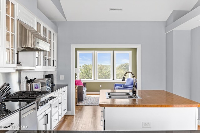 kitchen with exhaust hood, white cabinetry, a sink, and light wood finished floors