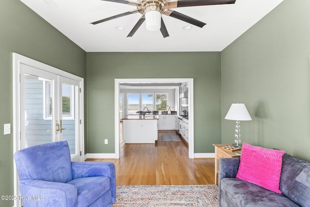 living area with baseboards, ceiling fan, french doors, and wood finished floors