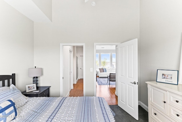 bedroom with dark wood-style flooring, a high ceiling, and baseboards