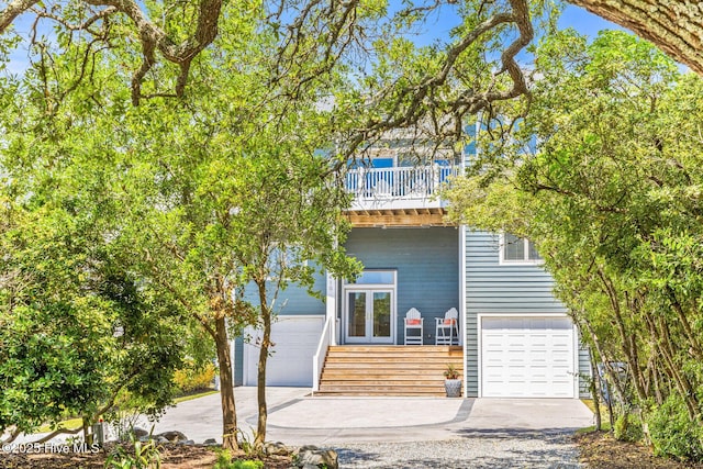 view of front of property with french doors, an attached garage, driveway, and a balcony