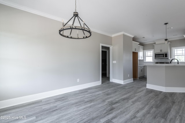 kitchen with white cabinets, light wood finished floors, stainless steel microwave, an inviting chandelier, and crown molding