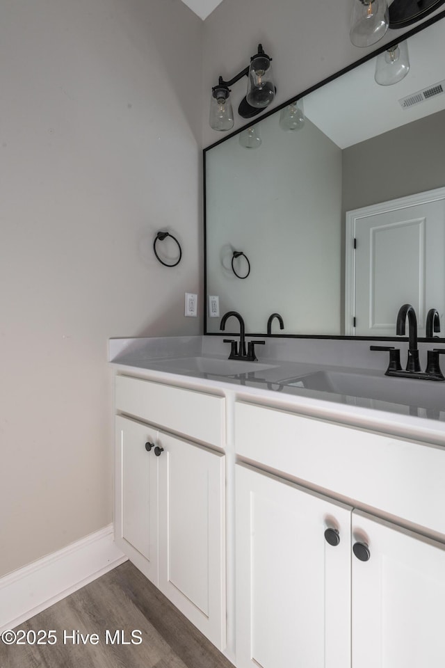 bathroom featuring wood finished floors, visible vents, a sink, and double vanity