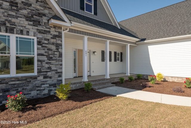 entrance to property featuring roof with shingles, a porch, stone siding, and board and batten siding