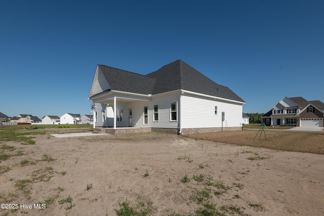 back of property with a porch, roof with shingles, and a residential view
