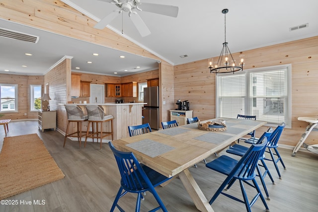 6621 W Beach Dr, Oak Island, NC 28465 - dining area featuring wooden walls, light wood-type flooring, vaulted ceiling, a chandelier, and a ceiling fan