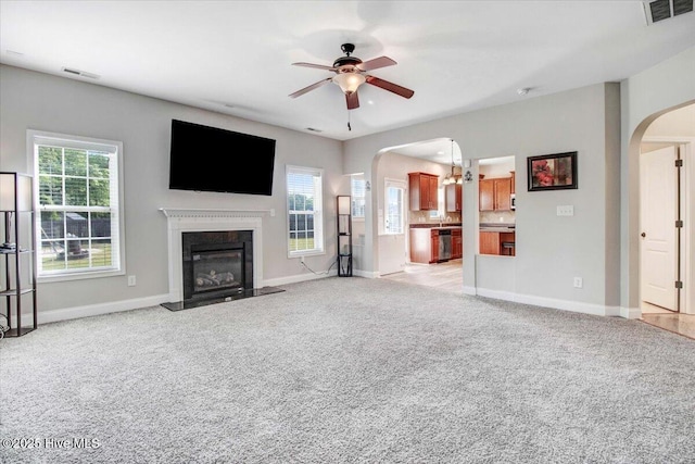  - unfurnished living room with arched walkways, a glass covered fireplace, visible vents, light colored carpet, and ceiling fan