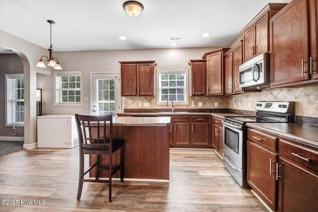  - kitchen with arched walkways, a sink, a breakfast bar, a kitchen island, and appliances with stainless steel finishes