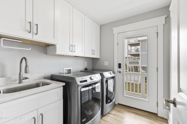 washroom featuring independent washer and dryer, a sink, light wood-style flooring, and cabinet space