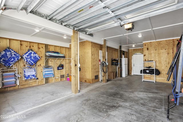 garage featuring freestanding refrigerator, wood walls, and a garage door opener