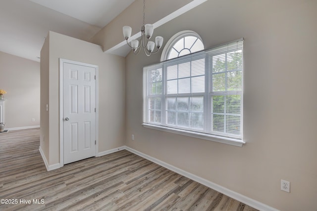 spare room with light wood-type flooring, baseboards, a chandelier, and vaulted ceiling