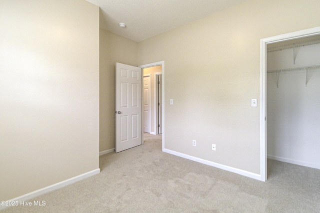 unfurnished bedroom featuring a walk in closet, carpet floors, and baseboards