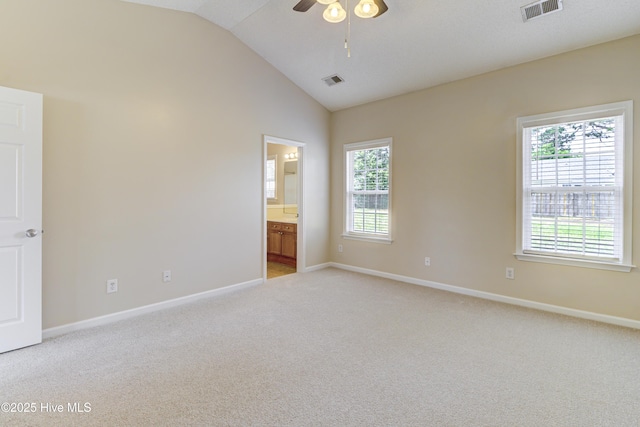 empty room featuring lofted ceiling, visible vents, ceiling fan, and light colored carpet