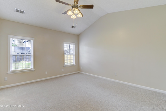 carpeted empty room with vaulted ceiling, visible vents, and a wealth of natural light